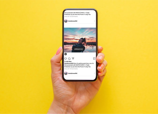a yellow background with a person's hand holding up a smartphone with an instagram feed on the screen