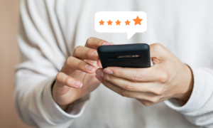closeup of a person holding a smartphone with a 5-star review bubble coming out of the screen