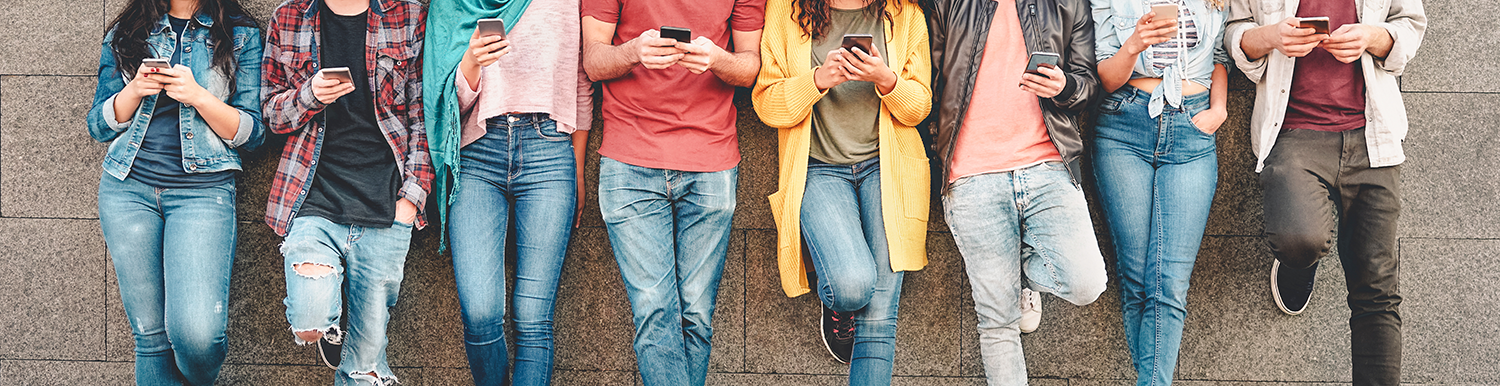 photo of multiple people's torsos, each leaning against a brick wall side-by-side and holding their own smartphones
