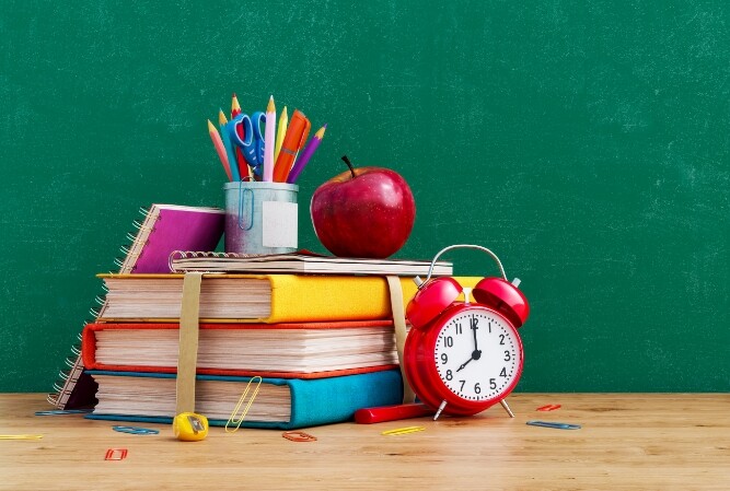 a pile of books and school supplies posed in front of a chalk board