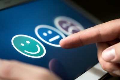 close-up photo of a hand choosing between a happy face and frowning face
