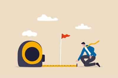 Business success measurement concept, smart businessman using measuring tape to measure the distance from the target flag.