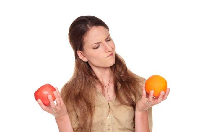 Isolated studio shot of a Caucasian businesswoman making a difficult choice between an apple and orange