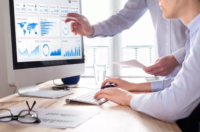 Two people looking at a computer screen displaying analytics reports.